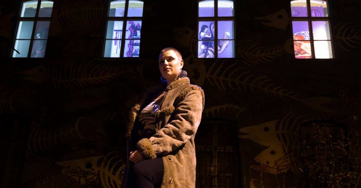 Lenča Malec - the author of the 2025 visual identity for the 26th International Feminist and Queer Festival Red Dawns. Lenča is photographed in front of her exhibition Orgy of Pixels at the Pešaki Night Gallery that was part of the festival. Photo by Nada Žgank.